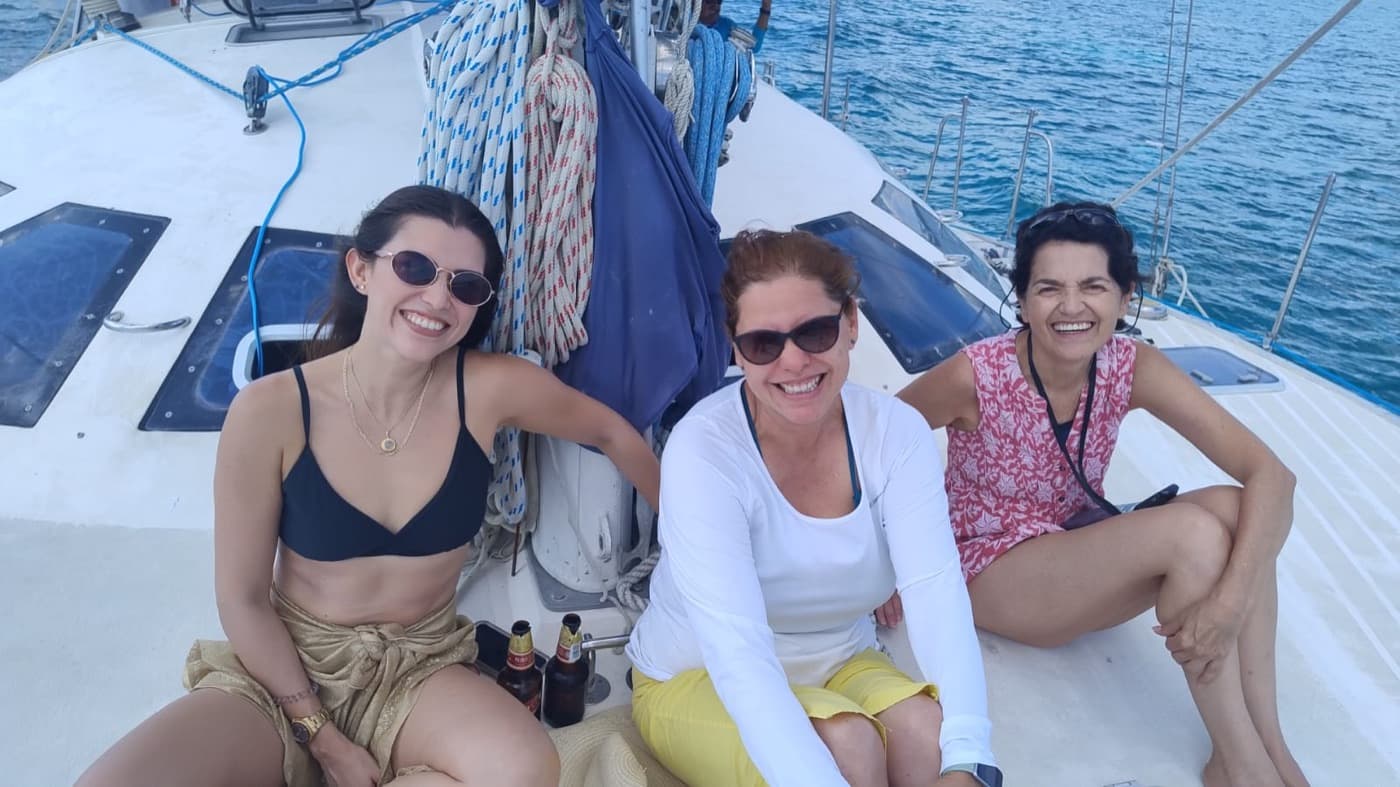 Tres huéspedes riendo juntas en la cubierta de un catamarán de vela