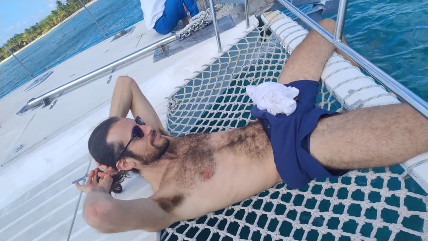 Un huésped recostado sobre la red de proa del catamarán, encima del agua