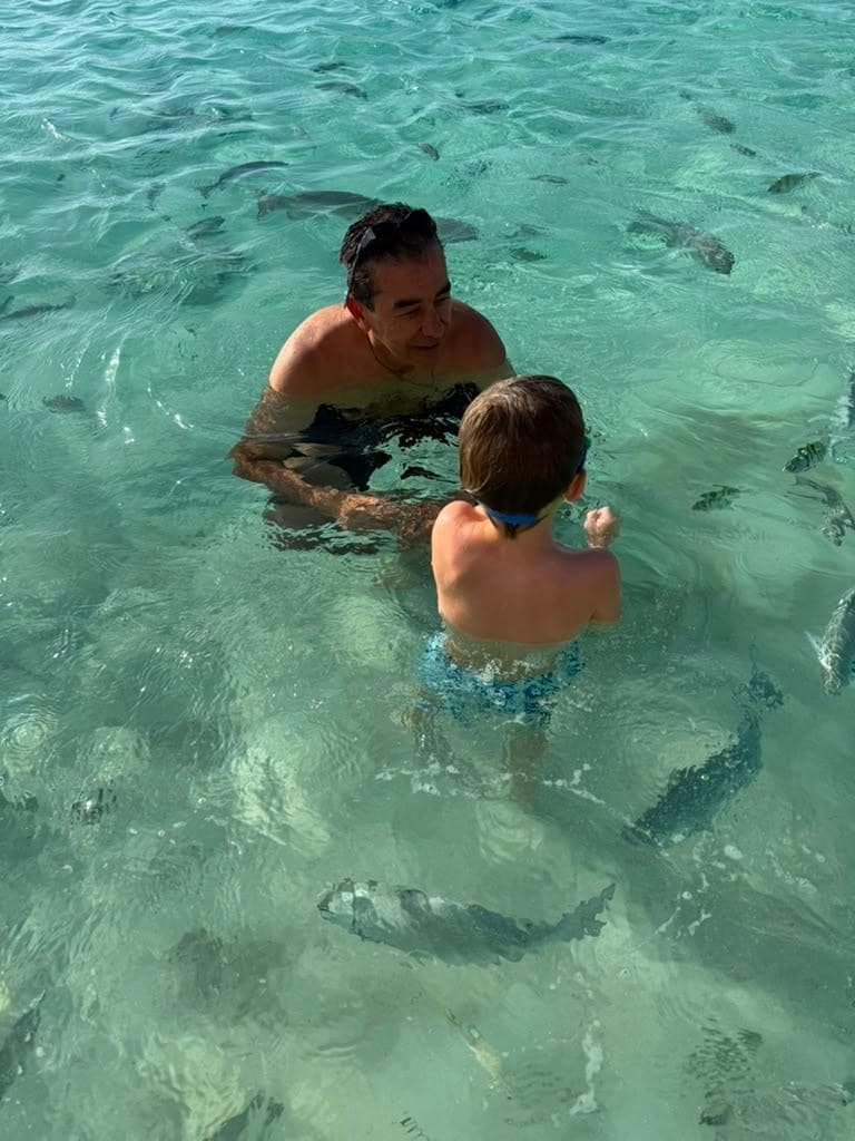 Un hombre y un niño de pie en agua clara rodeados de peces