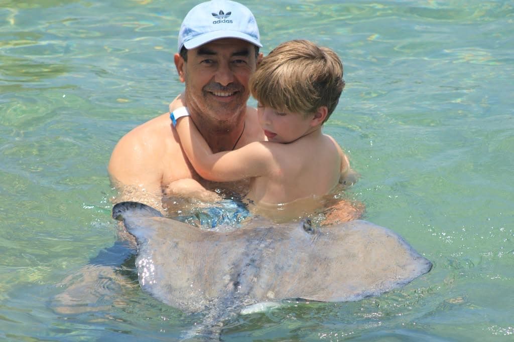 Un hombre mayor y un niño sostienen una raya en agua clara y poco profunda